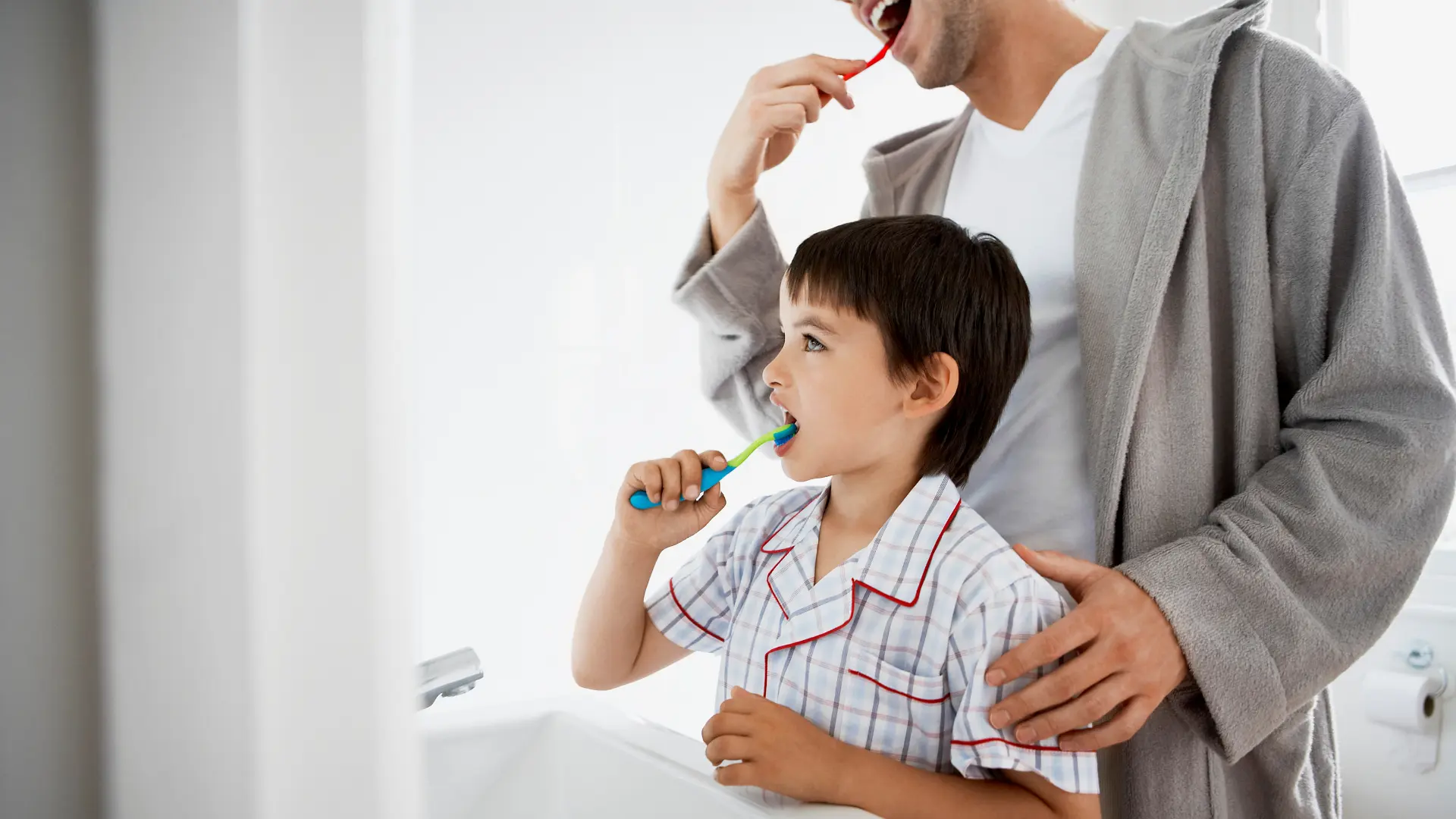 A father teaches his son good brushing habits, a key part of daily kids dental care to prevent cavities.